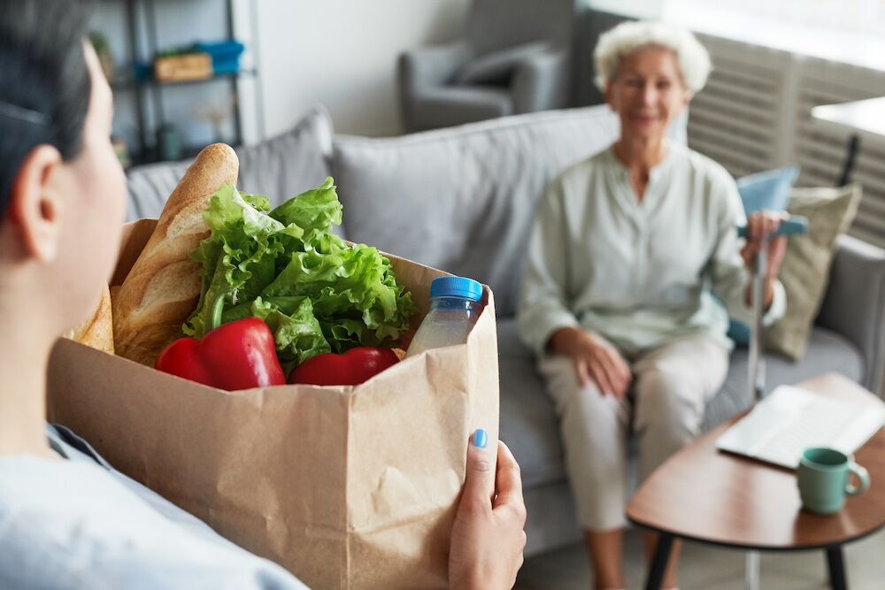 A woman working for the best senior care management in Michigan delivering groceries to a senior woman