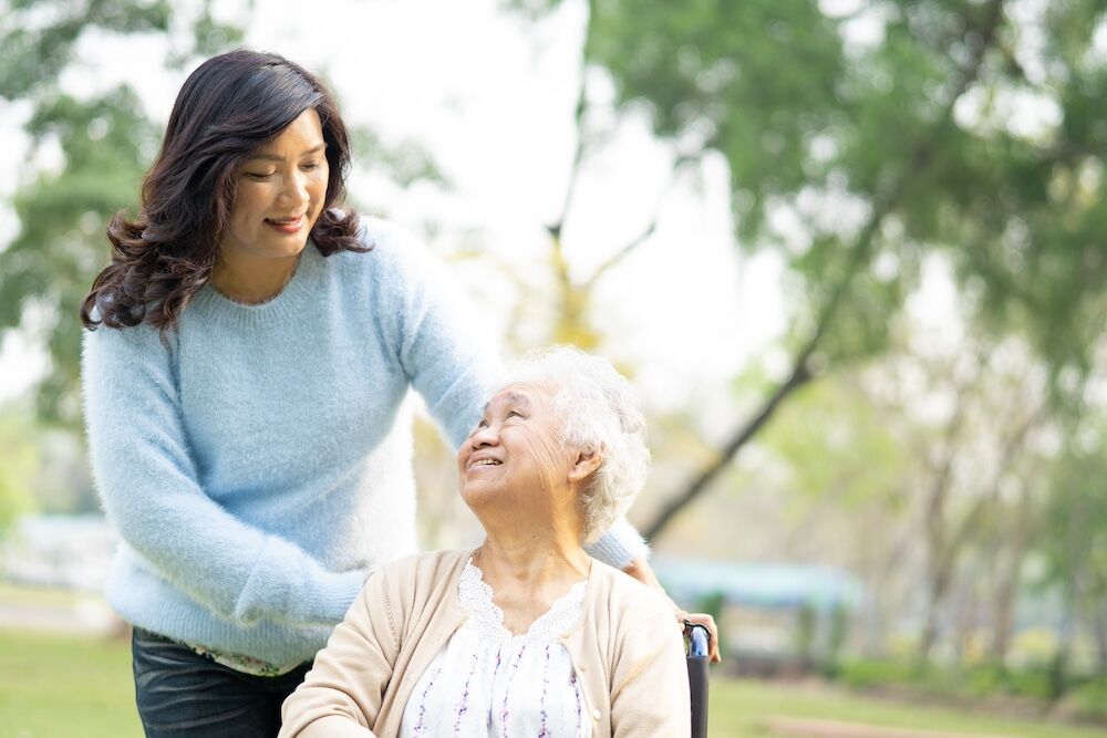 A senior woman in a wheelchair and her adult daughter go for a walk outdoors