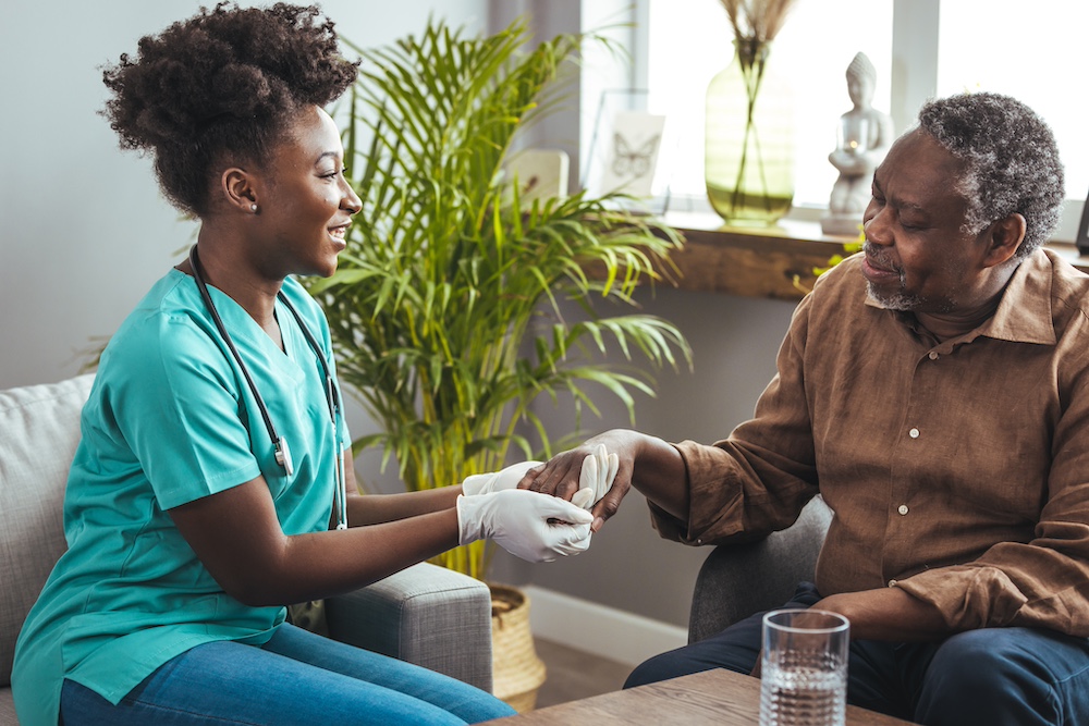 A senior man holds hands with his caregiver during a chat