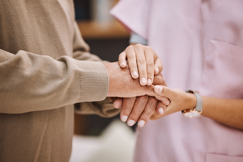 A senior man and a caregiver hold hands