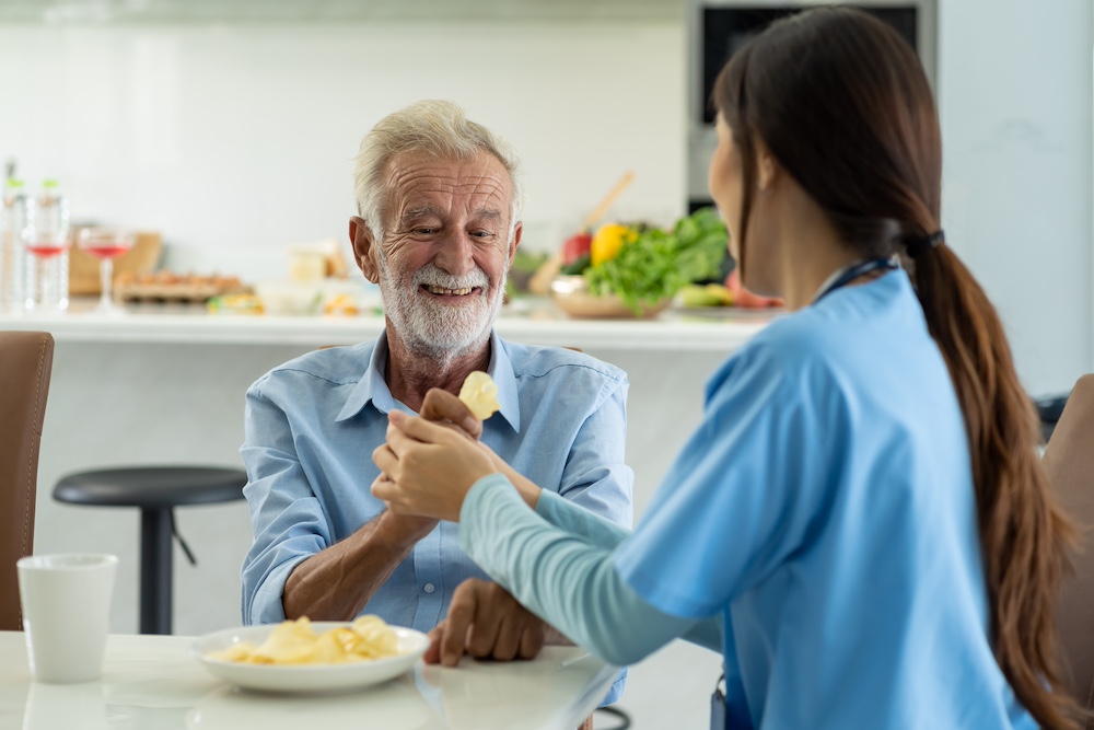 A caregiver assisting a senior man eating lunch
