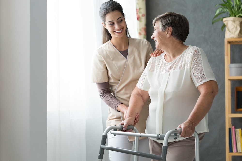 A smiling caregiver assists a senior woman who is using a walker