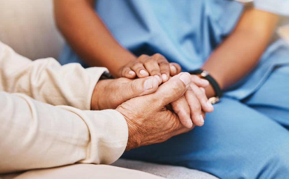 An up close photo of a senior man holding hands with a caregiver